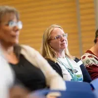 A faculty member from CWI listens to a reading while sitting in the audience.