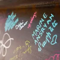 Signatures in teal, pink, white, and yellow are seen on a brown metal beam.