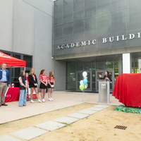 People attend the unveiling of a new artwork sculpture outside an academic building on a college campus.
