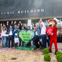 People attend the unveiling of a new artwork sculpture outside an academic building on a college campus.