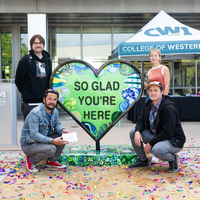 People attend the unveiling of a new artwork sculpture outside an academic building on a college campus.
