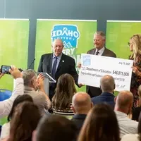 A speaker stands at a podium addressing an audience while giving a ceremonial check.