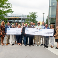 A group of dignitaries hold 3 ceremonial checks.