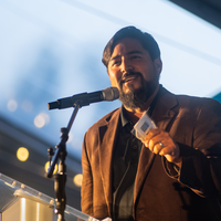 A man in a suit addresses the audience at a benefit dinner and auction.