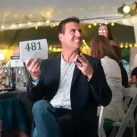 A man holds up a numbered sign while bidding in an auction.
