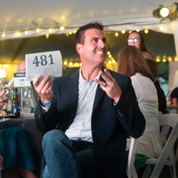A man holds up a numbered sign while bidding in an auction.