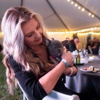 A woman holds a puppy at a benefit dinner.