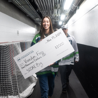 A smiling woman carries a $1000 ceremonial check down a hallway.