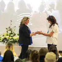 Students listen to speakers at a graduation and then receive their pins, signifying graduation.