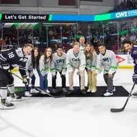 CWI President Gordon Jones drops the hockey puck on the ice surrounded by students.