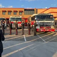 Uniformed firefighters standing at attention and saluting in front of fire engines at Nampa Fire Station during a ceremony.