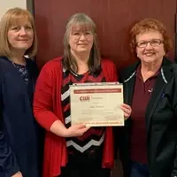 Student standing holding a Emerging Professionals certificate and standing next to instructors