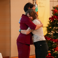 Two people hugging on a stage with decorated Christmas tree nearby