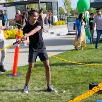 A smiling student prepares to swing a large mallet to test his strength at a yard game.