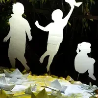 Silhouettes of three children appear against a dark background, surrounded by paper boats and soft lighting.