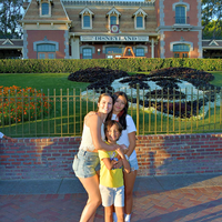 A mother and two children smile for the camera in front of Disneyland.