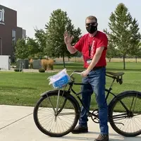 CWI staff member, Ross Hosking, handing out Be Safe, Be Mighty kits to students at the Nampa Campus Academic Building on a bike