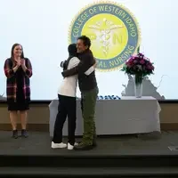 Two people hugging with a third clapping in the background