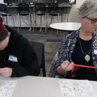 Two people sitting at a table making dream catchers