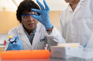 CWI student in safety glasses holding a small substance bottle in a lab