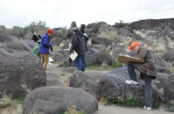 Students with clipboards studing giant rocks outside