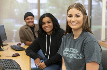 CWI students in a computer classroom sitting in a row looking at the camera