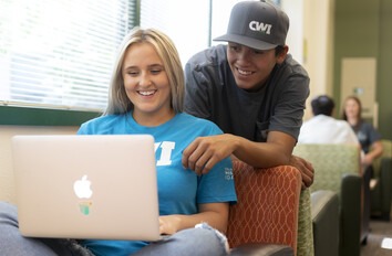 Two students smiling while looking at a laptop