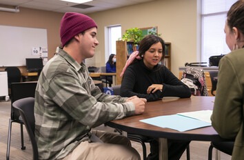 Three students sitting around a table in a classroom