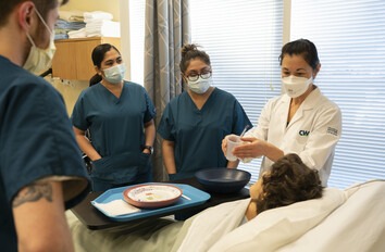 Group of CWI students in a classroom standing over a mannequin's bed