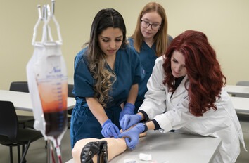 Instructor showing students how to take blood in a healthcare lab