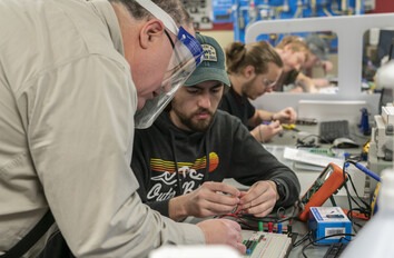 Instructor and student closely looking at electronic equipment