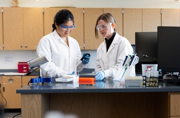 Two CWI students in lab coats and safety glasses in a lab