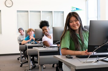 Students sitting at computers looking at the camera