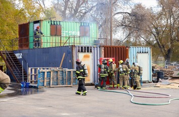 Students in fire suites working with fire hoses at large containers