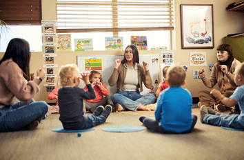 Teachers working with group of young children while sitting in a circle on the floor