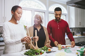 Family making salad in kitchen with older parent