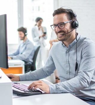 Person with headset in an office smiling at a computer screen