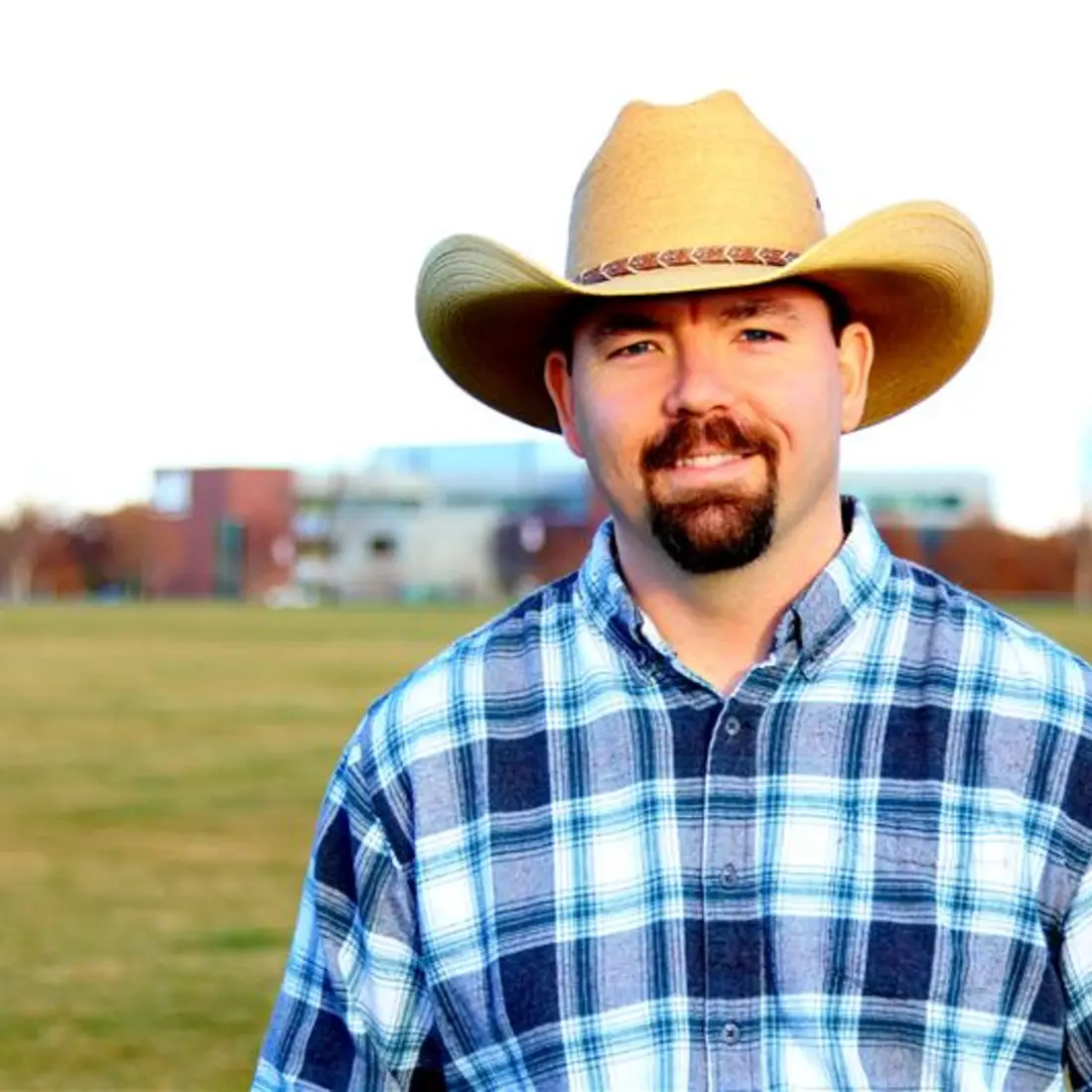 Man in cowboy hat in field with building behind him
