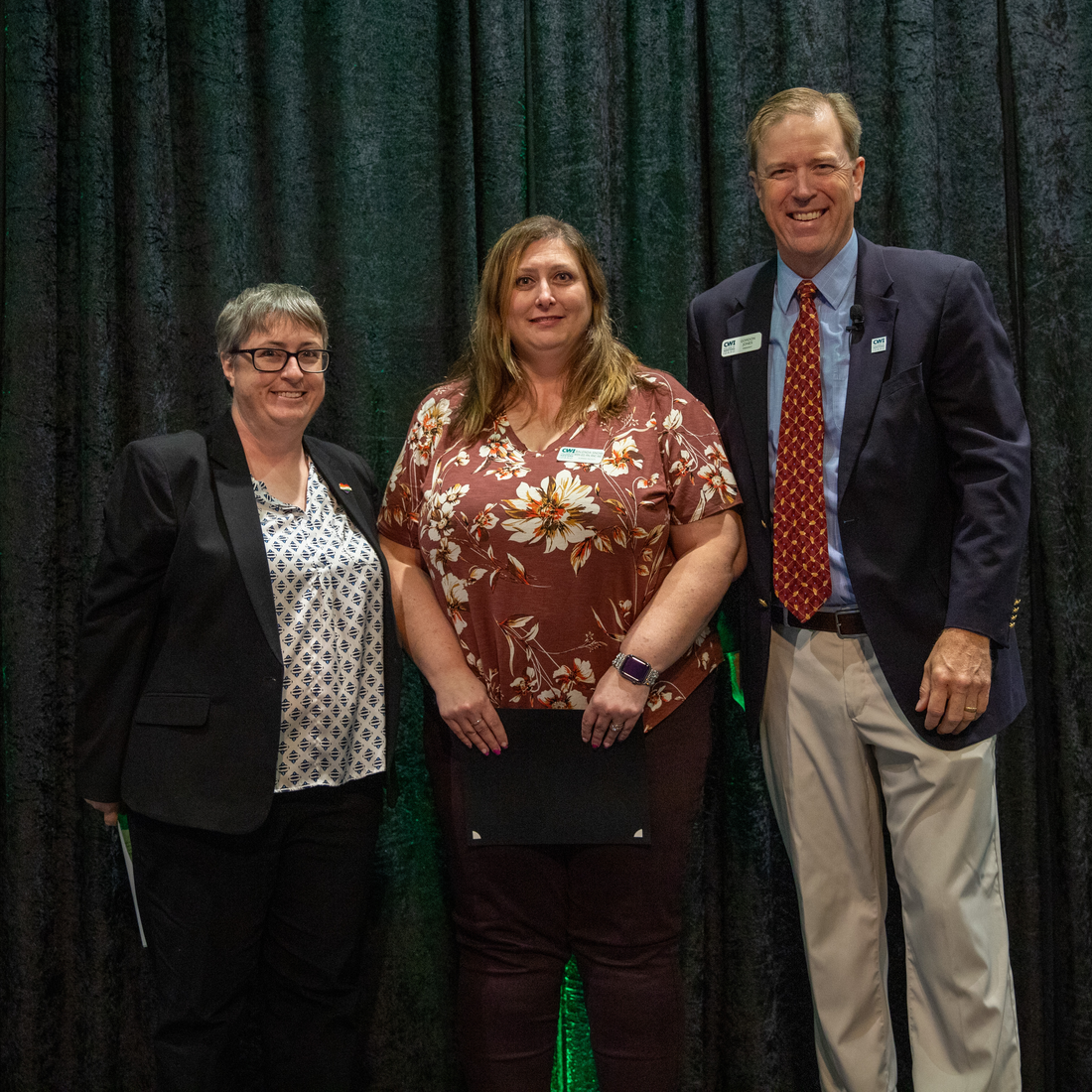 Three people stand in front of a curtain