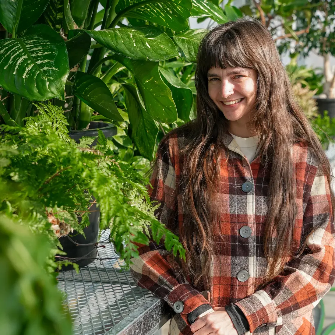 Student stands in greenhouse in front of several plants