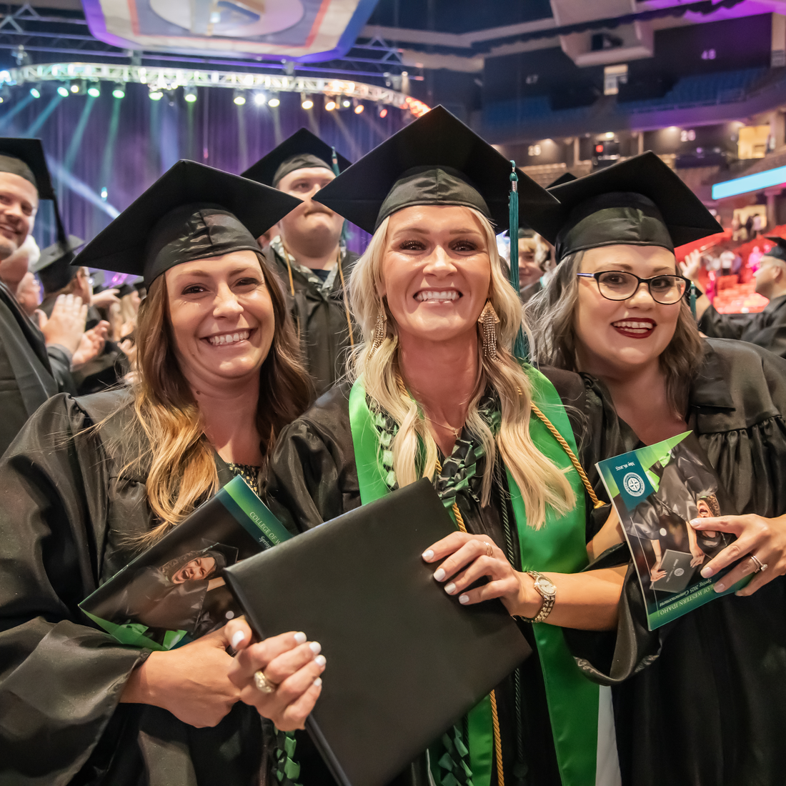 Three people with diplomas and in cap and gowns