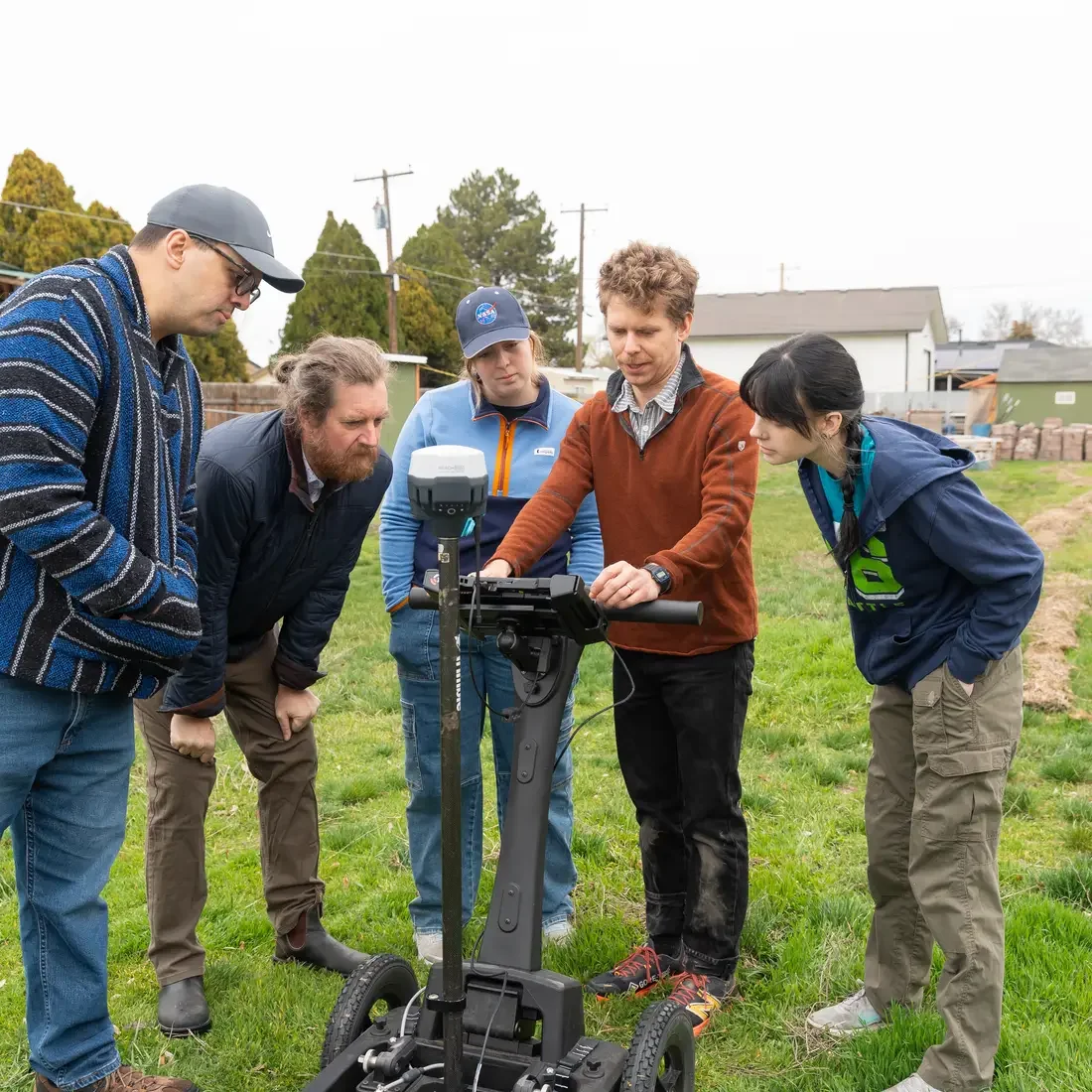 Five people stand on grass while looking at a screen 