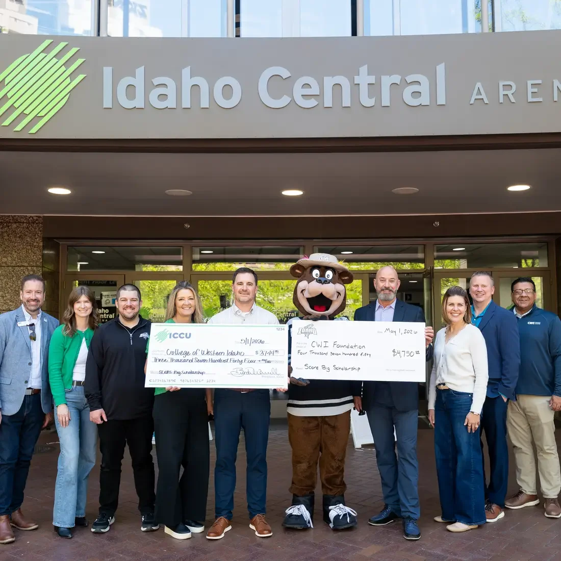 Group of people with bear mascot holding two checks