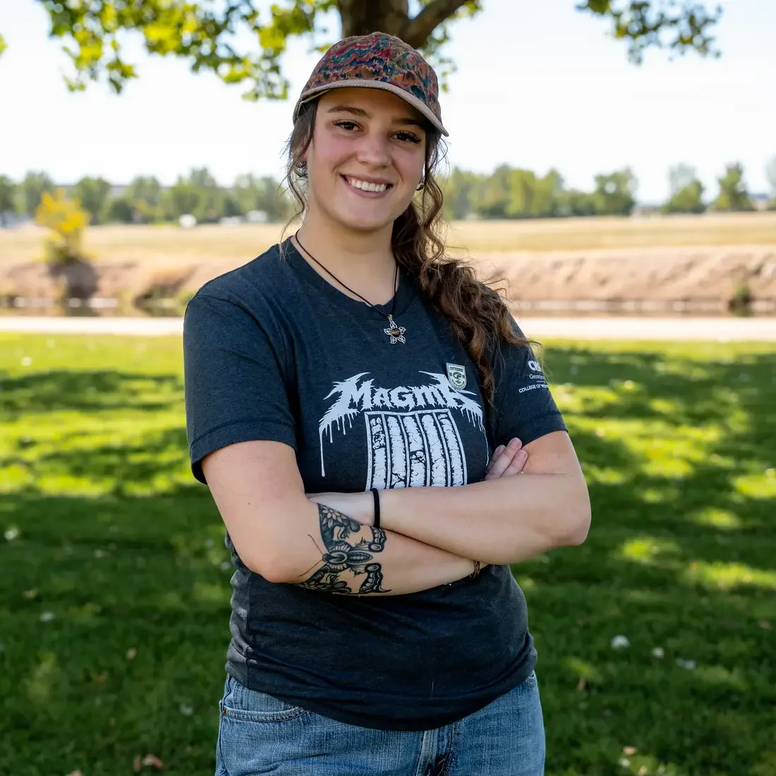 Person stands in front of tree and grass with arms crossed