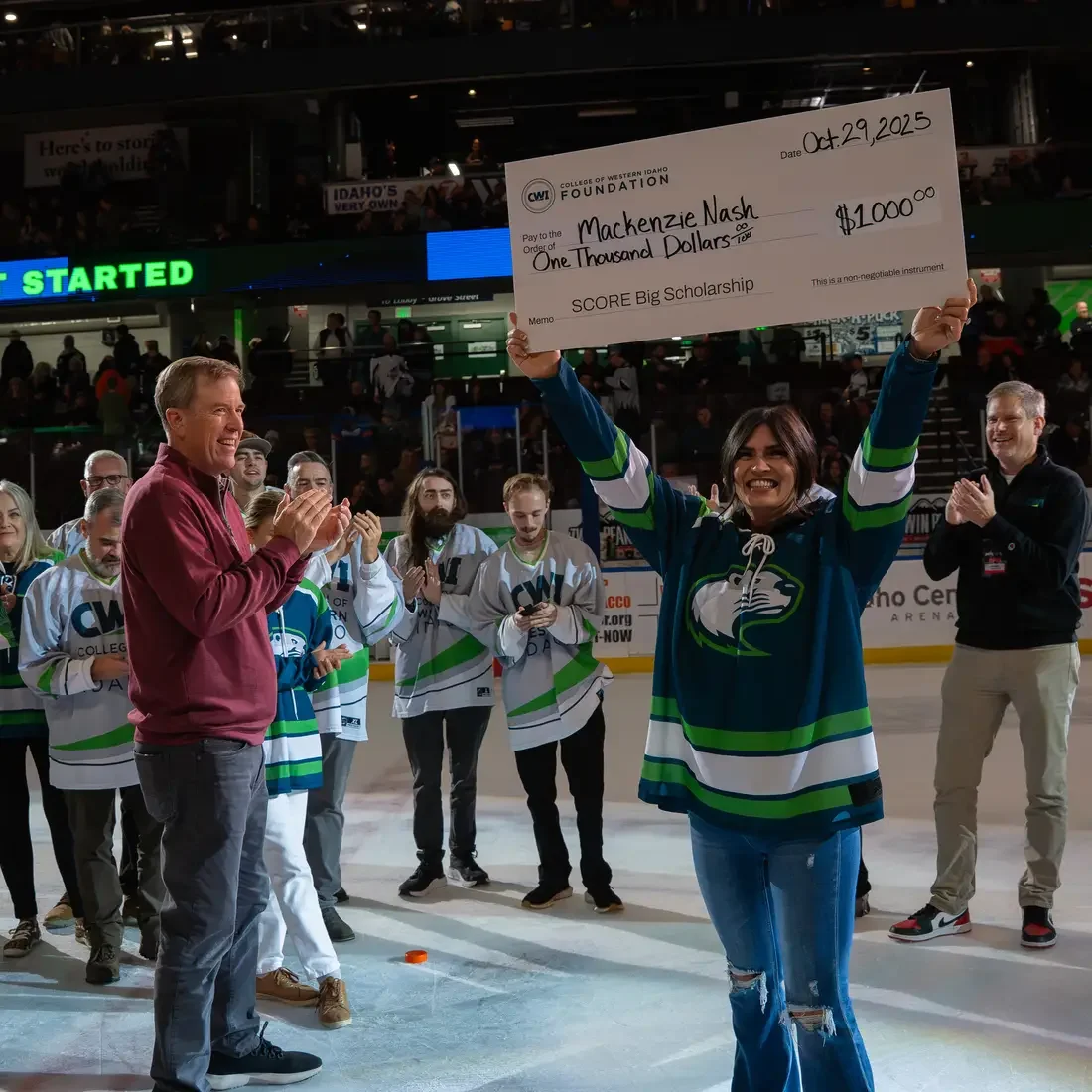 Student stands on hocky rink holding up large check with people surrounding them