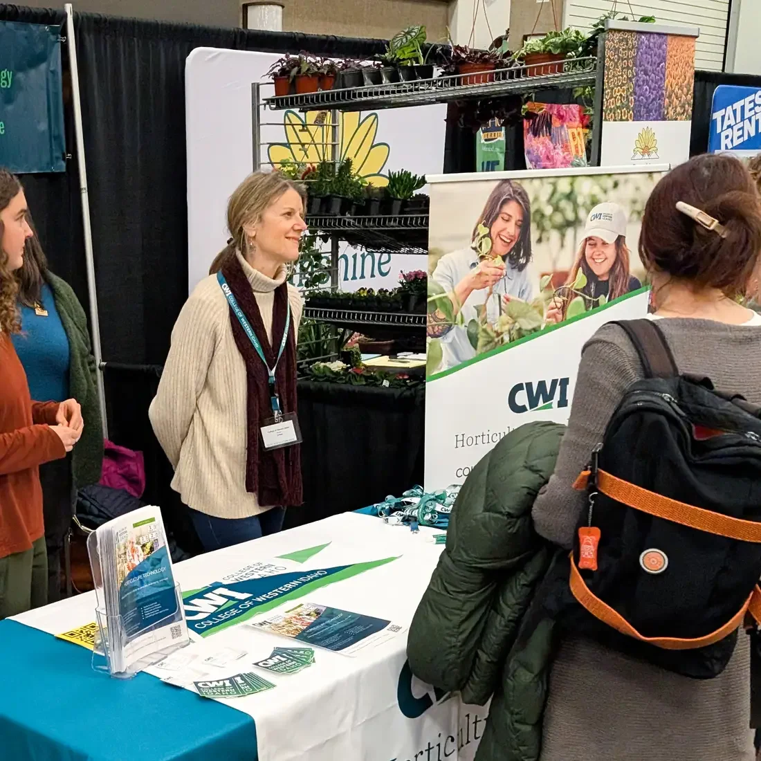Students speak with attendees of a conference from behind a booth table.