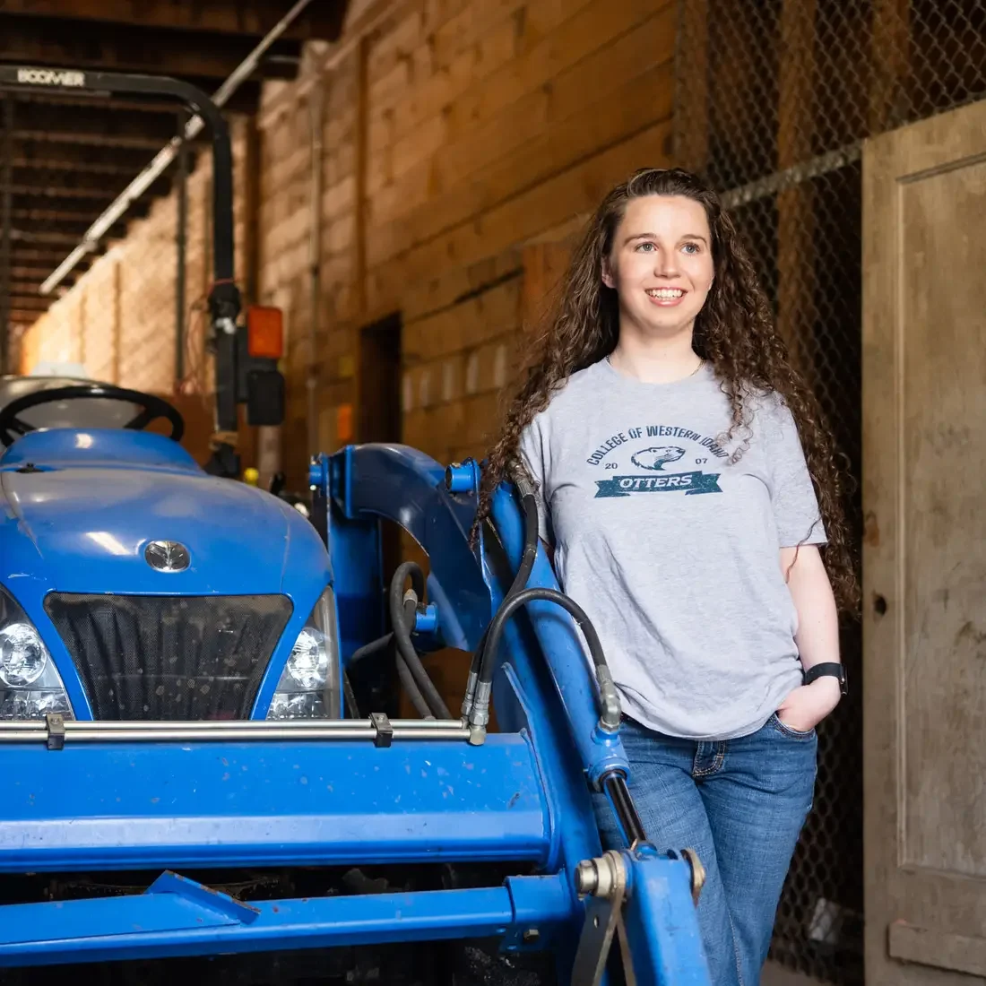 A student smiles next to a blue tractor.