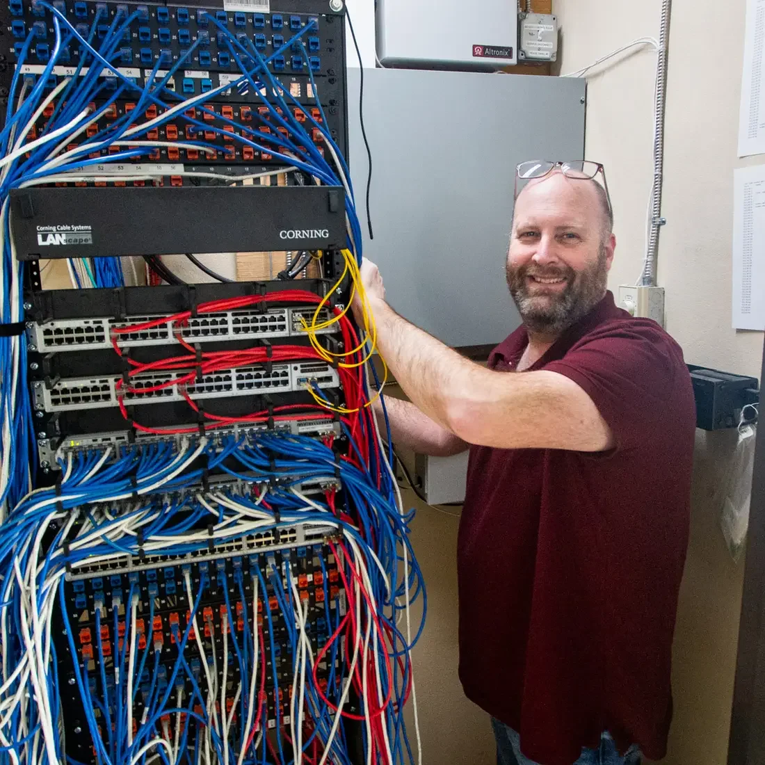 A portrait of William Alworth standing in a telcom closet surrounded by wires and ethernet cables.