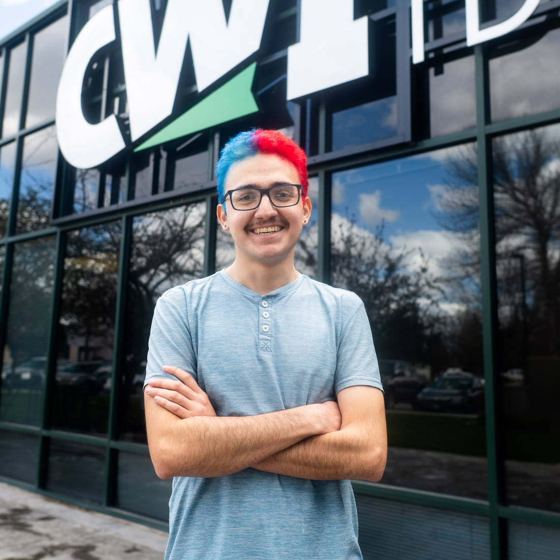 A student stands smiling in front of a building.