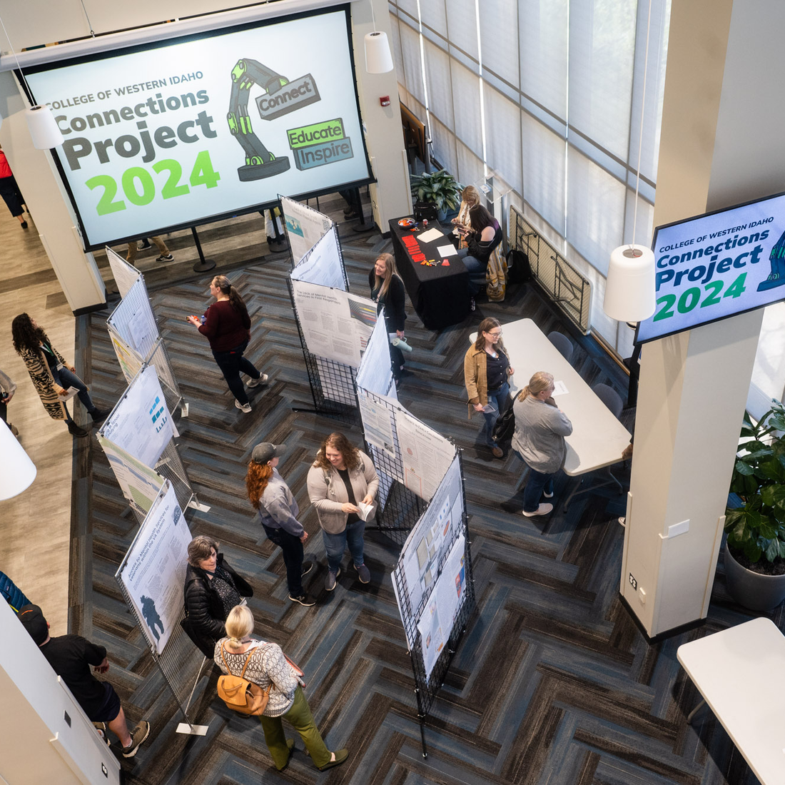 Students and members of the community browse research posters at an event. Screens display "Connections Project 2024."